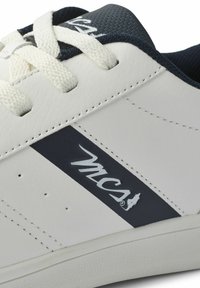 Hvit sneaker med marineblå detaljer, teksturert overdel, flate lisser, logopatch og perforeringer for ventilasjon langs siden. Mykt materiale.
