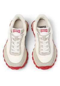 Baskets blanches et beiges avec une semelle en caoutchouc rouge, présentant un dessus en tissu texturé, un système de laçage et le logo "CAMPER" sur la languette.