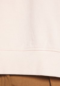 Ljusrosa sweatshirtmaterial med en mjuk textur och ribbad nederkant. Synlig sömdetalj i botten, parat med brunt tyg under.