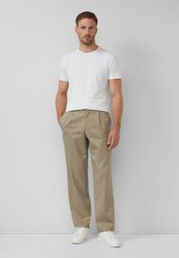 Biały t-shirt z krótkim rękawem w połączeniu z jasnobeżowymi spodniami. Model nosi białe sneakersy. Gładka tkanina o swobodnym kroju i czystych liniach.