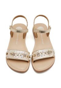 Sandalias de color dorado con suela plana. Presenta una correa de tela adornada con perlas y acentos dorados. Correa ajustable en el tobillo.