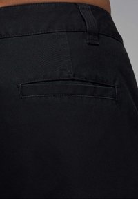 Sorte stofbukser med en glat overflade, tætsiddende pasform og en enkelt baglomme med en ren stikkant.