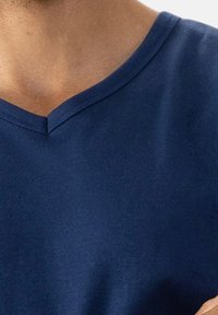 Close-up van de nek en bovenste borst van een persoon in een donkerblauwe V-hals shirt.