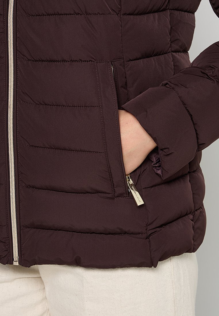 Veste en duvet bordeaux avec des coutures horizontales, fermeture éclair à l'avant et poches latérales. Elle présente des poignets élastiques et une texture lisse et matelassée.