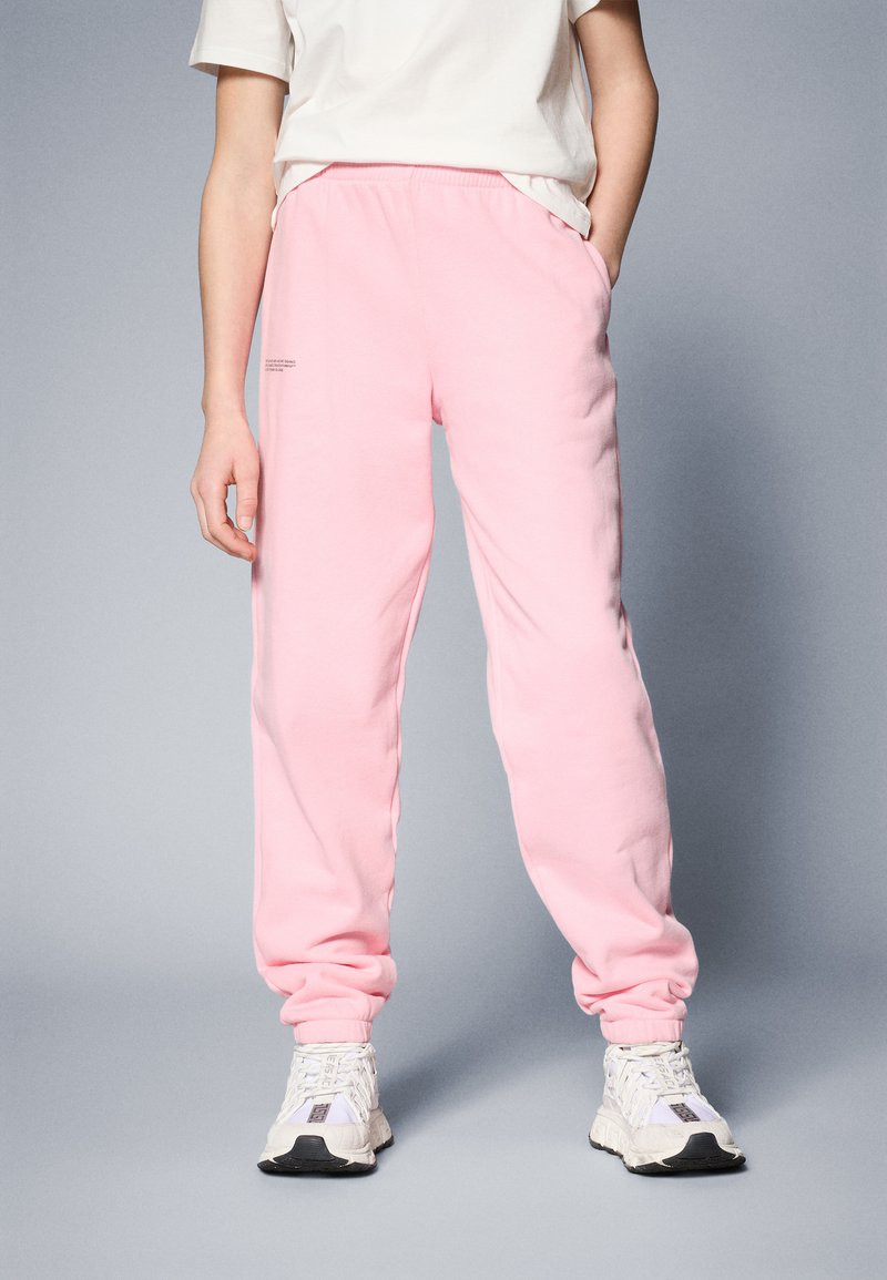 Pantalones de chándal rosa hechos de un material suave, con una cintura y puños elásticos. Combinados con zapatillas blancas, que presentan un diseño sencillo.