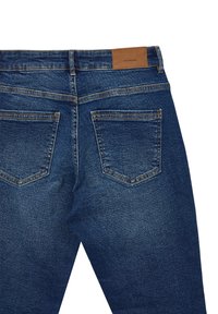 Vue arrière d'un jean en denim bleu foncé avec deux poches arrière et un patch en cuir marron de la marque sur la ceinture.