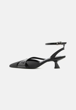 Schwarzer Slingback-Kitty-Heel mit spitzer Spitze, dünnem Knöchelriemen und asymmetrischen Kreuzriemen vor weißem Hintergrund.