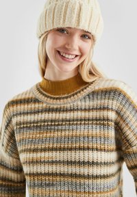 Sweter w paski w kolorze beżowym, brązowym i szarym o fakturowanym wykończeniu; posiada ściągacz w kolorze musztardowym; zestawiony z kremową czapką.