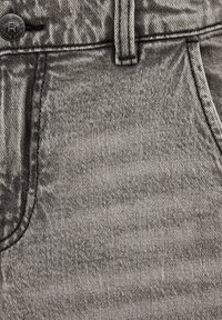 Tejido de mezclilla gris mostrando un primer plano de los detalles del bolsillo y la cremallera, con una textura sutil y costuras que delinean los contornos del bolsillo.