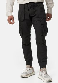 Pantalones cargo negros con puños elásticos y múltiples bolsillos laterales. Hechos de tejido ligero con una textura suave y cintura con cordón.