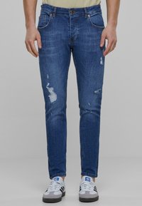 Vyblednuté modré denimové džínsy so slim fit strihom, s poškodenými detailami a s gombíkovým zapínaním. Skombinované s bielymi a sivými športovými topánkami.