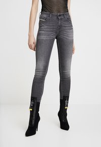 Jeans ajustados grises con un patrón desgastado, con cintura alta, cinco bolsillos y combinados con botas de tobillo negras ajustadas.