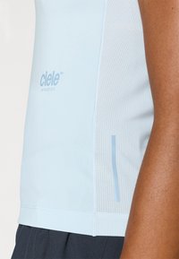 Camisola atlética azul claro com um tecido suave, painéis laterais em malha, logotipo discreto e um design ajustado, exibindo um estilo moderno para vestuário ativo.