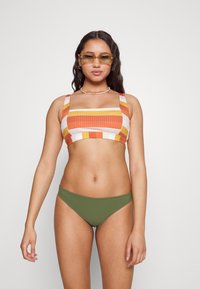 Top de bikini às riscas em laranja, amarelo e branco, com alças largas; combinado com calções de bikini verde-oliva. Tecido suave, design justo.