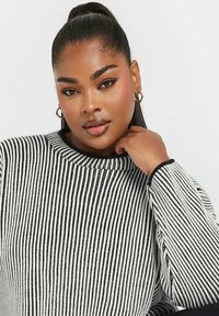 Maglione a righe nere e bianche in maglia con scollatura rotonda e polsini a costine. Tessuto liscio, fit rilassato. Carnagione chiara con orecchini a cerchio.