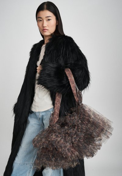 Braune und durchsichtige Tülltasche mit Rüschentextur, mit einem gemusterten Tragegurt und silbernen Kettendetails. Das Modell trägt einen schwarzen Pelzmantel und Jeans.