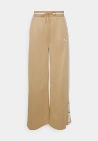 Pantalones de chándal anchos color tan con cintura ajustable por cordón, botones de presión en los laterales y un logo blanco de Puma en la parte frontal izquierda.