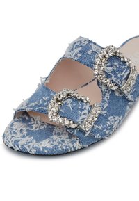 Blue denim mules with frayed texture, open toe design, and dual rhinestone buckles for embellishment. Smooth interior lining.