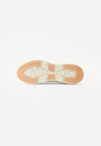 Sko såle med en teksturert hvit gummibase med oransje detaljer, omrissede mønstre for grep, og fremtredende merkevarebokstaver.