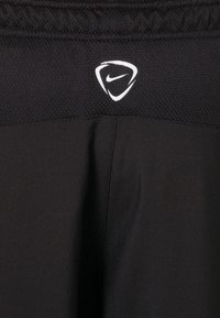 Czarne legginsy sportowe wykonane z elastycznej, gładkiej tkaniny z teksturowanym pasem. Posiadają białe logo Nike na pasie.