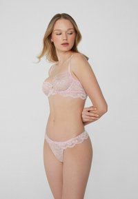 Soutien-gorge en dentelle rose et string assorti avec des motifs floraux, des bords festonnés et des fines bretelles, mettant en valeur des détails complexes et une texture délicate.