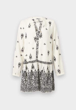 Tunique blanche à manches longues avec des motifs floraux et géométriques noirs complexes, col à nouer, et une bordure à motifs à l'ourlet et à la taille.