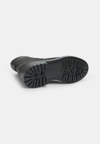 Bota negra con un empeine texturizado y suela de goma estriada que presenta tacos profundos para tracción y durabilidad.