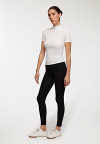 Biała, krótko rękawowa bluzka z półgolfem wykonana z prążkowanej tkaniny, zestawiona z czarnymi legginsami i białymi butami sportowymi z gumową podeszwą.