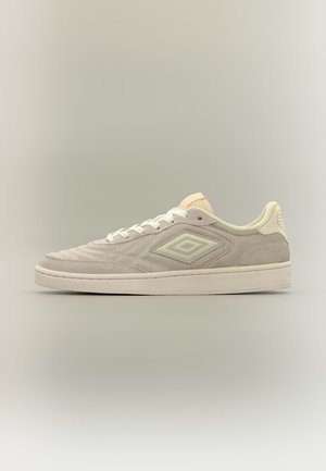 Vista laterale di una sneaker in camoscio beige con lacci bianchi e logo a doppio diamante su sfondo neutro.