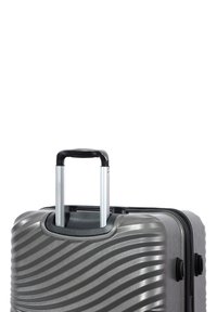 Hard-shell suitcase in metallic gray with textured wave pattern, featuring a black telescoping handle and dual wheels for mobility.