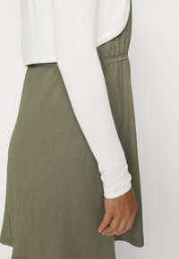 Haut blanc ajusté à manches longues avec texture côtelée, associé à une jupe ample vert olive avec une ceinture froncée et un motif texturé subtil.