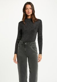 Maglietta nera a maniche lunghe con trama a coste e collo alto, abbinata a jeans grigi a vita alta con tasche frontali e cuciture a contrasto.