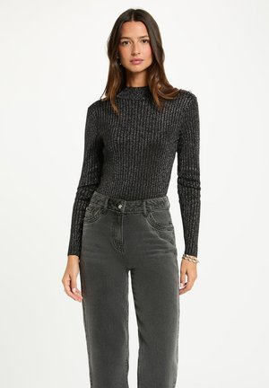 Maglietta nera a maniche lunghe con trama a coste e collo alto, abbinata a jeans grigi a vita alta con tasche frontali e cuciture a contrasto.
