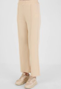 Light beige, wide-leg pants made from soft material with a high elastic waistband and contrasting side seams, paired with beige sneakers.