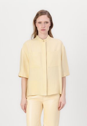 Camicia a maniche corte con colletto in leggero tessuto giallo, dotata di due tasche sul petto. Texture liscia e taglio dritto, con chiusura a bottoni.
