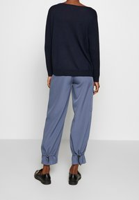 Pull marine avec côtés côtelés, coupe ample, associé à un pantalon bleu clair avec poignets élastiques et des chaussures noires faciles à enfiler.