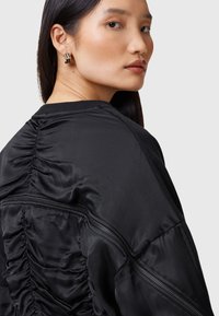 Giubbotto bomber nero con texture arricciata e zip a vista. Presenta un colletto tondo e maniche allungate, leggermente voluminose.