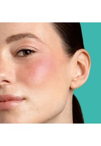 Nahaufnahme eines Gesichts mit glatter Hautstruktur, einem natürlichen, hellrosa Rouge auf der Wange und einem neutralen Hintergrund.