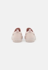 Hellrosa Sneaker mit einem strukturierten Lederfinish, flachen Sohlen und einer Schlaufe an der Rückseite, mit dem Brandnamen "GUESS" geprägt auf der Ferse.