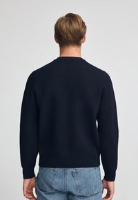 Marinblå stickad tröja med rund hals, ribbade ärmslut och nederkant; texturerad design på tyget; bärs med ljusa denimjeans.