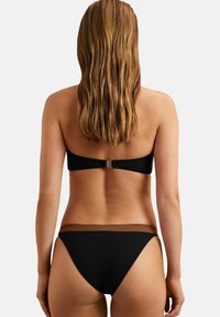 Juodas bikinis su bepečių viršumi, turinčiu auksinį užsegimą, ir žemai nuleidžiamais apatiniais su ruda akcentų juosta. Lygus, tamprus audinys.