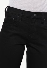 Černé džínové kalhoty mají slim fit střih, pět kapes a zapínání na knoflík. Látka má hladkou texturu s mírným leskem.