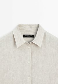 Jasnoszary, w paski polo z klasycznym kołnierzykiem, trzema guzikami i etykietą tekstową. Wykonane z miękkiej, teksturowanej tkaniny, idealne na co dzień.