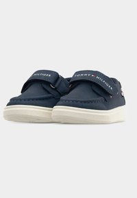 Παπούτσια από κανβά σε ναυτικό μπλε με λευκές ελαστικές σόλες, διαθέτουν ιμάντα με βέλκρο και λογότυπο στα λουριά. Στρογγυλεμένο σχέδιο στο μπροστινό μέρος.