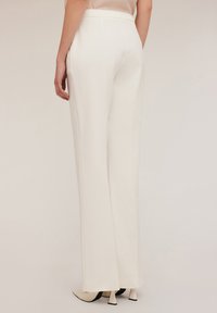Pantalones ajustados blancos con un corte recto, que presentan una textura suave y una cintura alta. Combinados con tacones negros de punta.