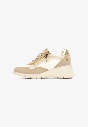 Zapatilla deportiva beige y crema con acentos dorados, tejido texturizado, cordones y detalle de cremallera lateral; suela gruesa y ligera con patrones de tracción.