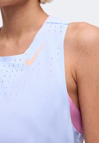 Близък план на човек, носещ светлосин безръкавен топ на Nike с малки вентилационни отвори и прасковено лого на Nike на гърдите.