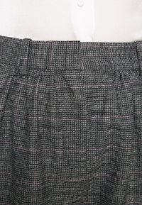 Pantalons à carreaux gris et noirs avec des accents roses, présentant un design plissé, une taille avec passants de ceinture et un tissu tissé texturé.