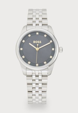 Montre-bracelet en argent avec un cadran rond gris, des accents dorés et huit marqueurs ressemblant à des diamants. Elle possède un boîtier en acier inoxydable et une couronne.