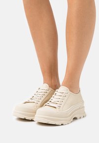 Beige sukad, mis on valmistatud siledast nahast, paksu tekstuuriga tallaga ja ümarate varvastega disain. Minimalistlik stiil koos diskreetsete õmblustähtedega.